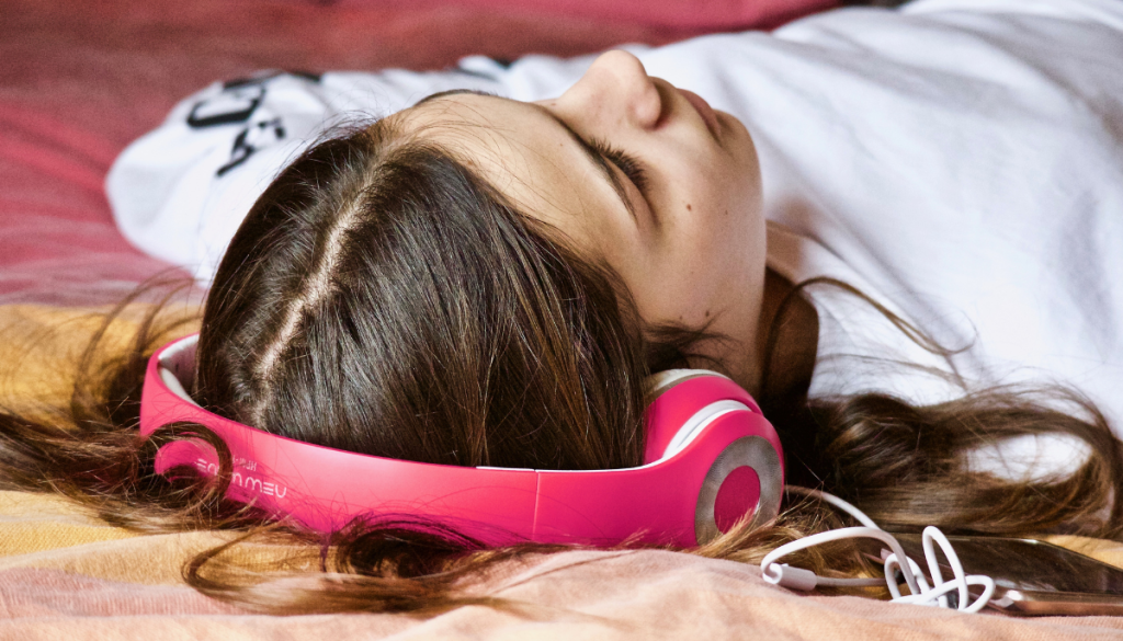 A young girl led on her bed listening to music.