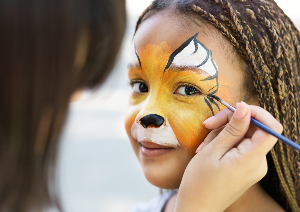 A young girl getting a orange butterfly painted on her face by a face painting professional.