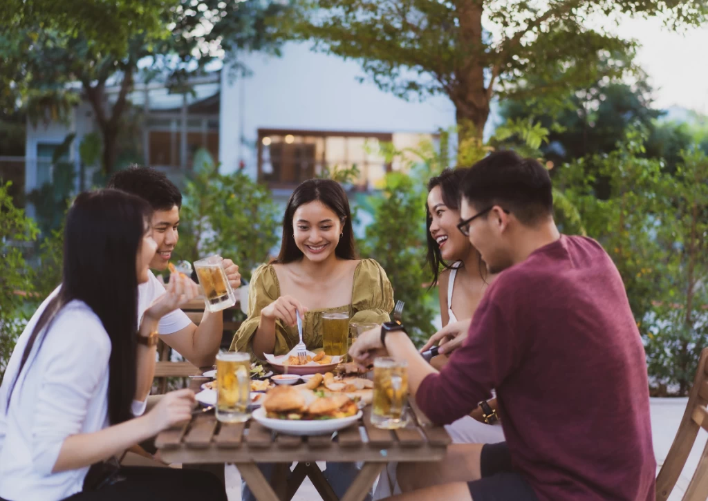 5 friends sitting around a wooden table for a outdoors garden party as their summer event idea.