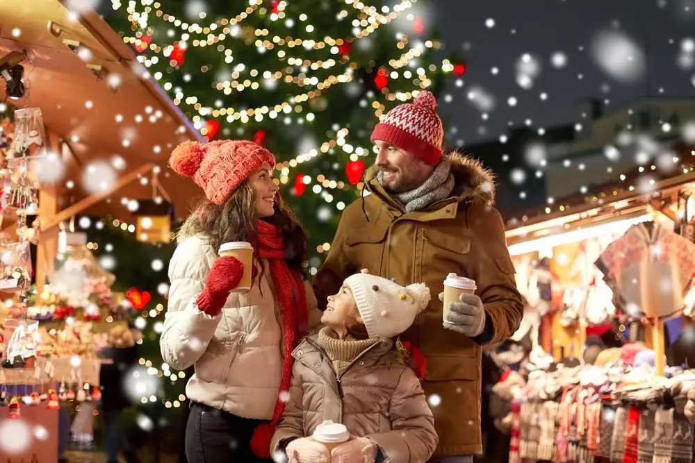 Family enjoying hot drinks at a snowy Christmas market.